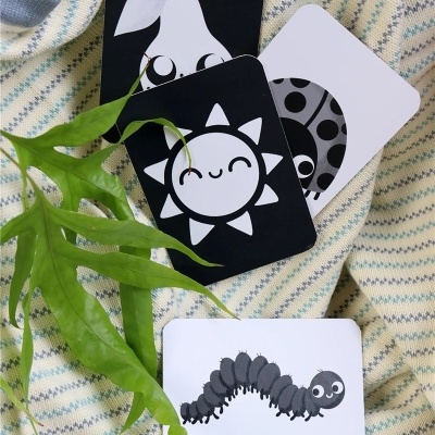 quatro cartões ilustrados a preto e branco com imagens de pêra, sol, joaninha e centopeia sobre tecido riscado com folha verde