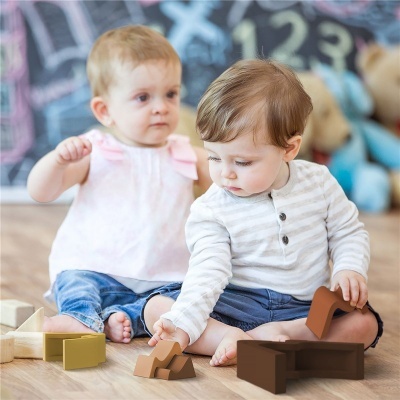 Bebés a brincar com blocos de madeira no chão com fundo de quadro negro e peluches.