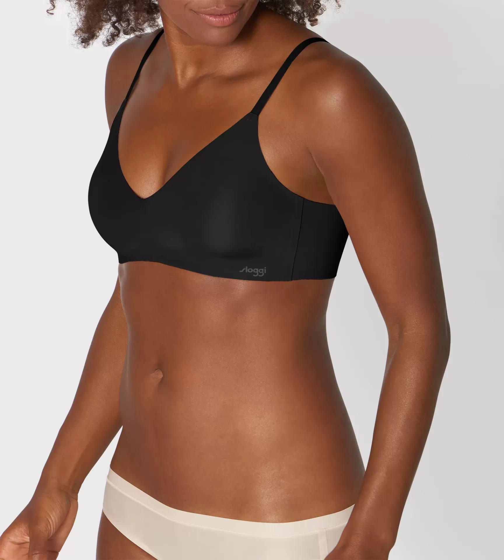 Soutien preto liso com alças finas e etiqueta 'sloggi' na lateral, usado por modelo.