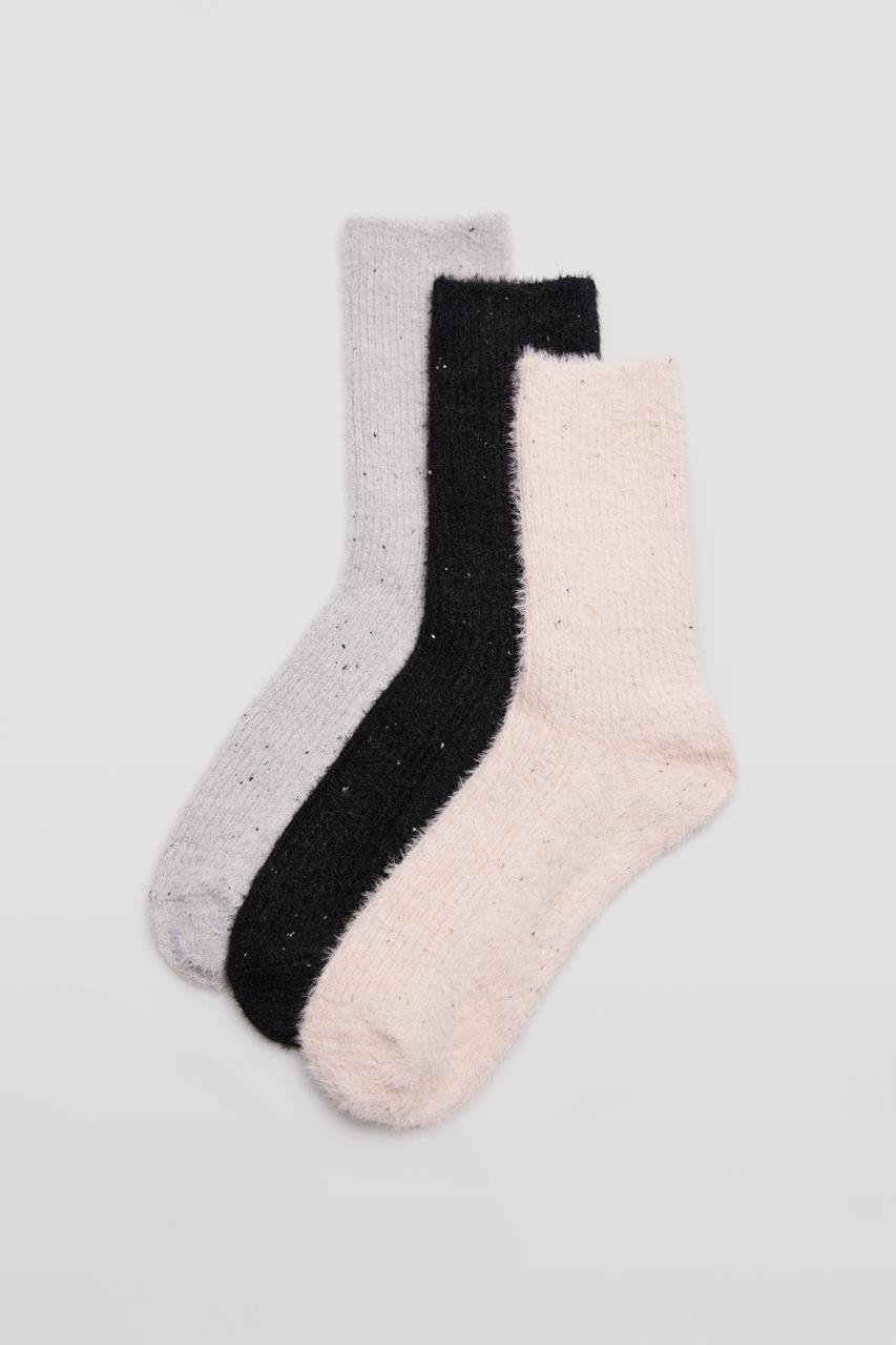 Três pares de meias felpudas em cinzento claro, preto e bege sobre fundo cinza claro