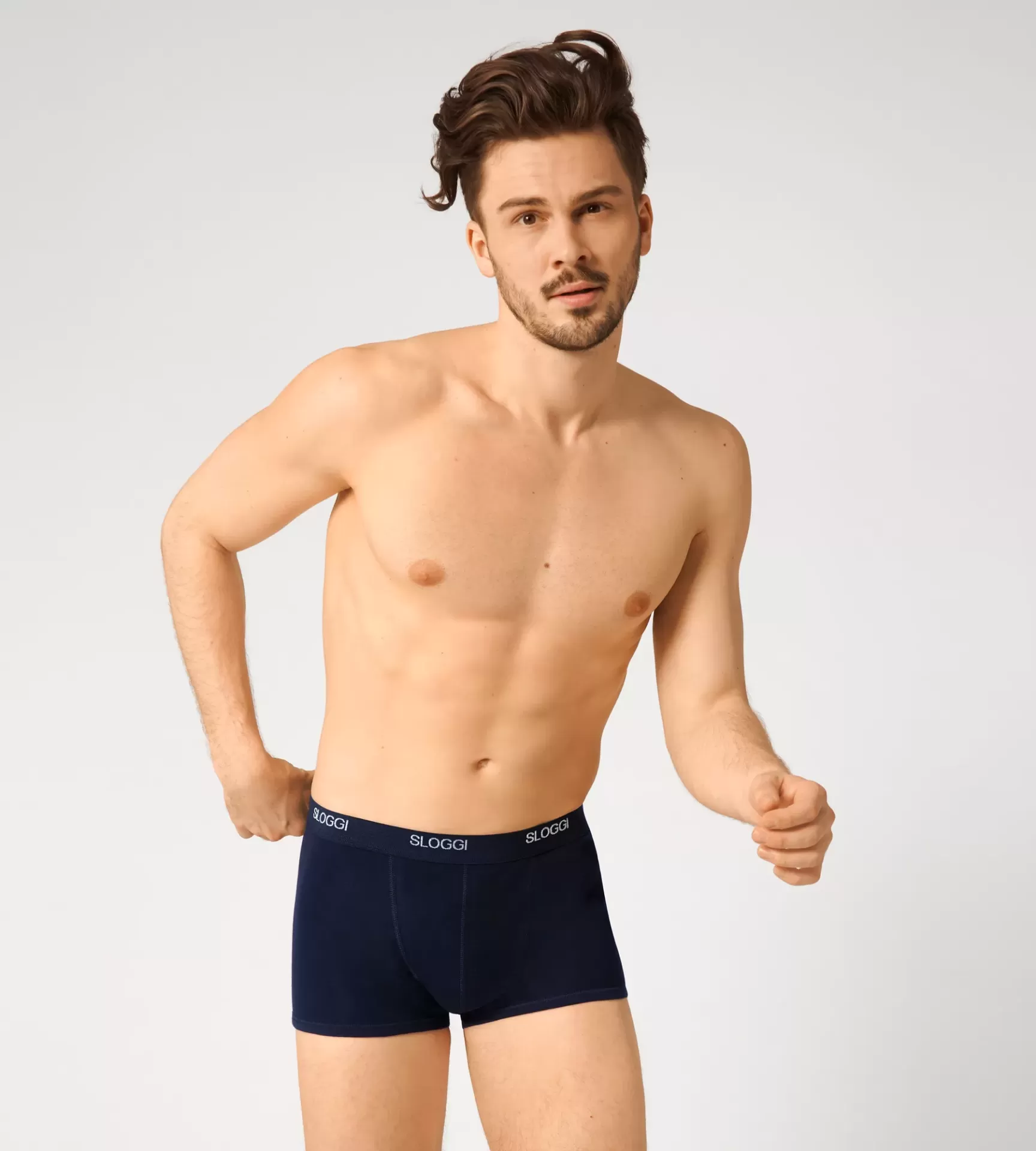 Homem com cueca boxer azul escuro com faixa preta e texto branco 'SLOGGI'