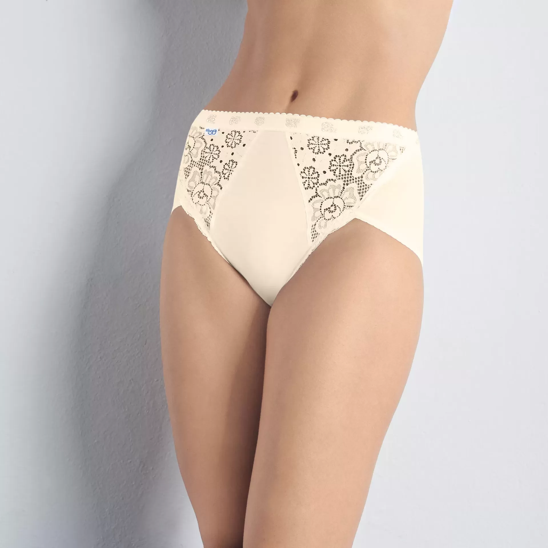 Calças de cintura alta bege com renda floral frontal em parede branca