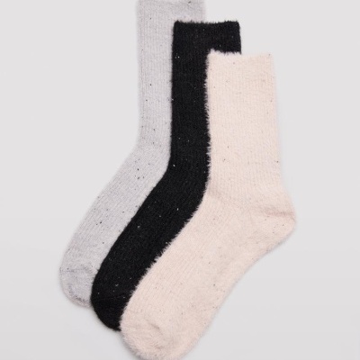 Três pares de meias felpudas em cinzento claro, preto e bege sobre fundo cinza claro