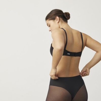 Mulher vista de costas com roupa interior preta, fundo branco.