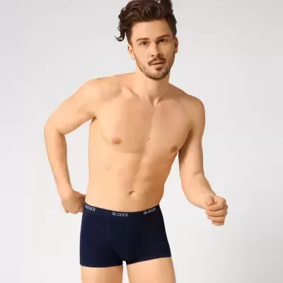 Homem com cueca boxer azul escuro com faixa preta e texto branco 'SLOGGI'
