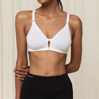 Soutien branco com recorte circular e calças pretas, mulher de pé em fundo bege