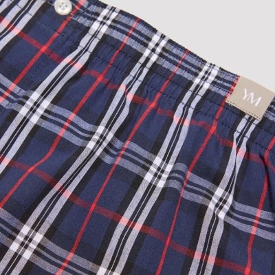 Peça de vestuário xadrez azul, vermelho, branco e preto com botões brancos na cintura elástica