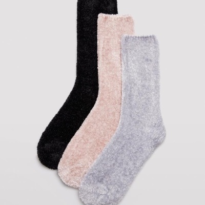 Três pares de meias felpudas em preto, rosa claro e cinza sobre fundo cinza