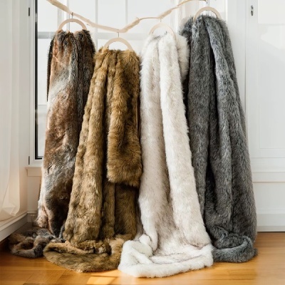 Quatro mantas de pelo sintético em castanho, bege, branco e cinza penduradas