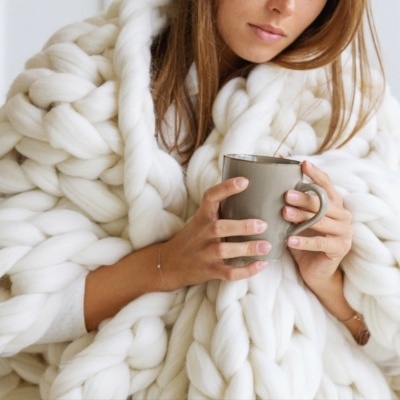 Mulher embrulhada em cobertor branco grosso segurando caneca cinza
