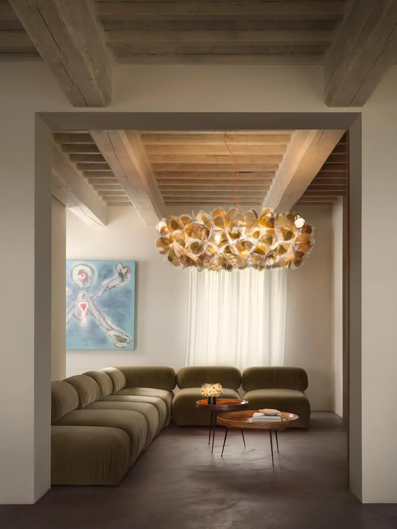 Lustre decorativo dourado moderno numa sala com sofá verde e mesas de apoio.