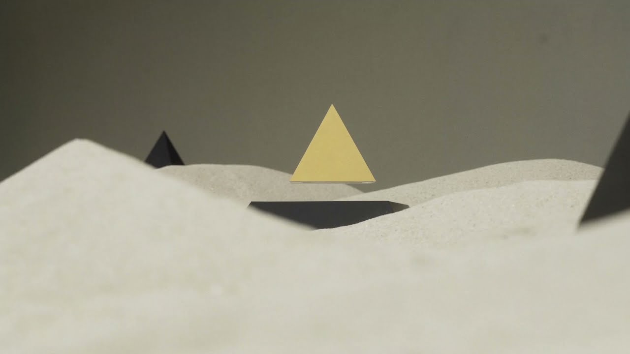 FLYTE PY Pirâmide amarela flutuando sobre superfície branca com pirâmides negras ao fundo