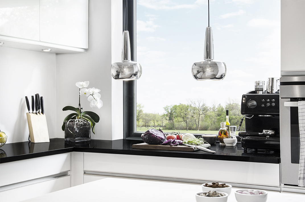 CLAVA Cozinha moderna com bancadas pretas, armários brancos, utensílios e planta junto a uma janela grande