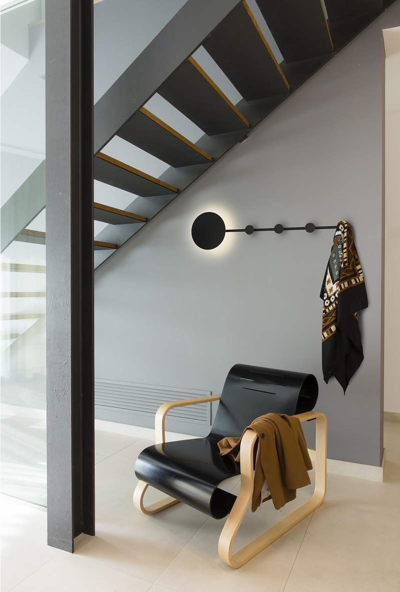 HAN LED Cadeira moderna em madeira clara e preto com casaco castanho, cabide preto com lenço decorativo pendurado na parede cinza sob escada