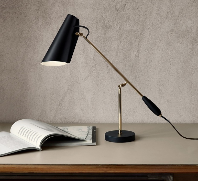 BIRDY Candeeiro de mesa preto e dourado numa mesa com livro aberto e parede cinza de fundo