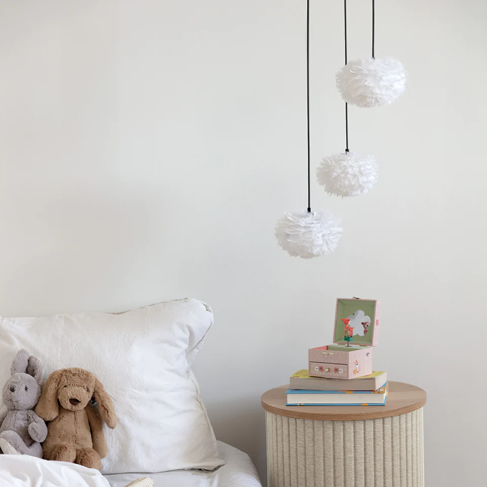 Quarto com cama branca, peluches, mesa de cabeceira redonda e três candeeiros brancos pendurados