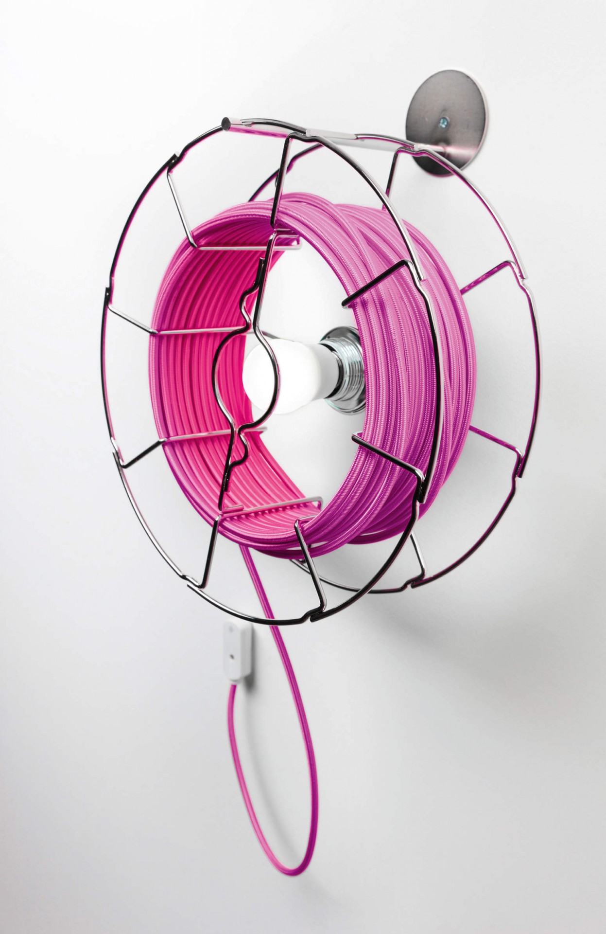 ARIANNA Cabo elétrico rosa enrolado num suporte metálico circular na parede