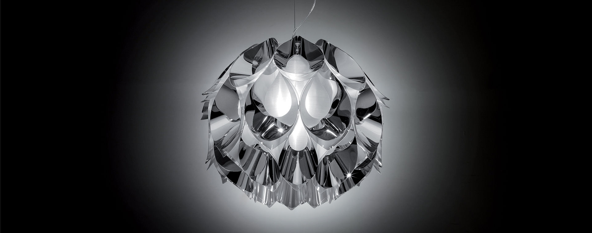 FLORA Lâmpada pendente metálica prateada com design curvo, suspensa contra fundo escuro.