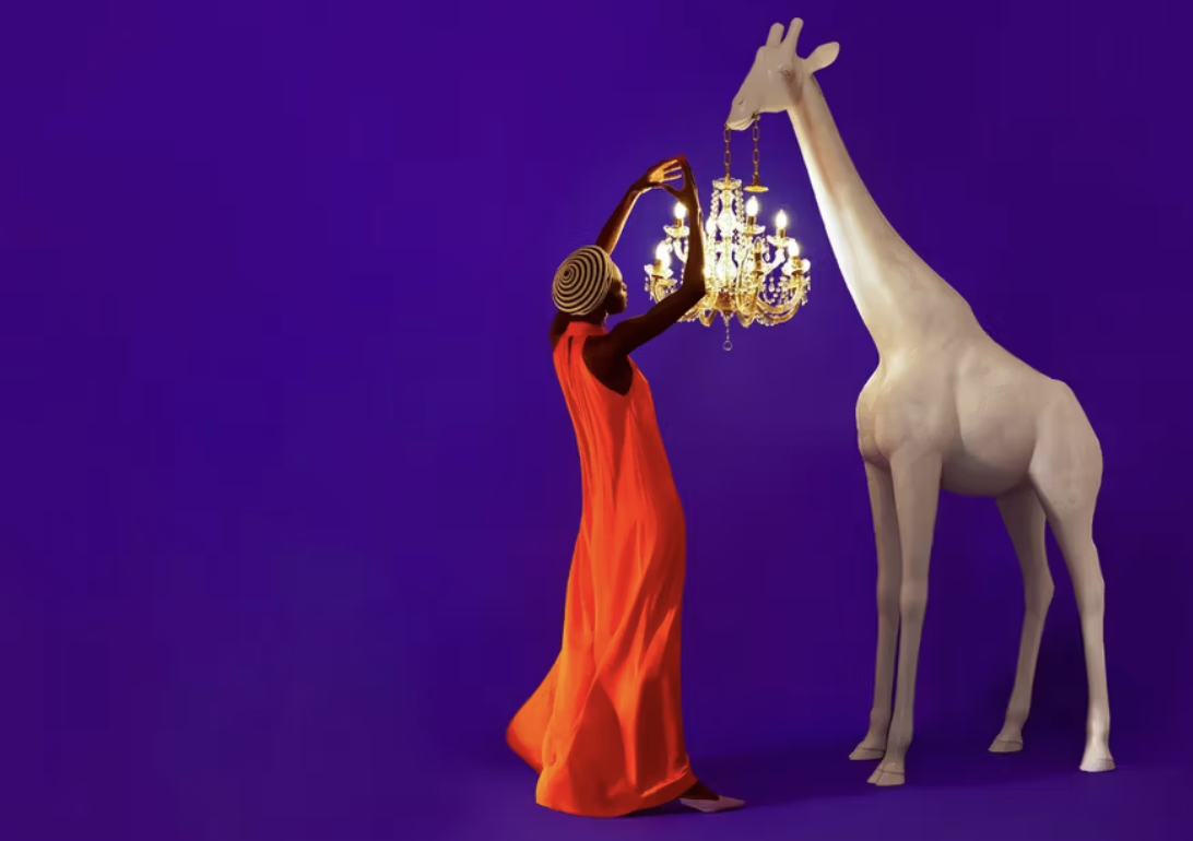 GIRAFFE IN LOVE M Indoor Pessoa com vestido laranja a ajustar candelabro pendurado de escultura de girafa