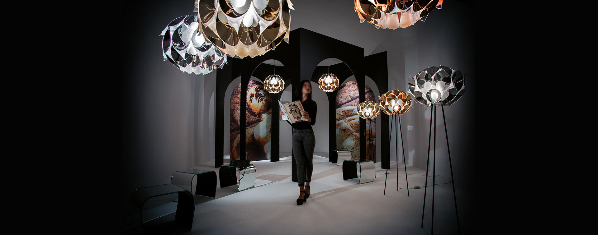 FLORA Luminárias modernas em branco, dourado e cobre com mulher segurando quadro ao centro, fundo escuro com arcos