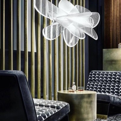 Sala com cadeiras estofadas pretas com padrão geométrico, mesa dourada redonda e luminária branca suspensa