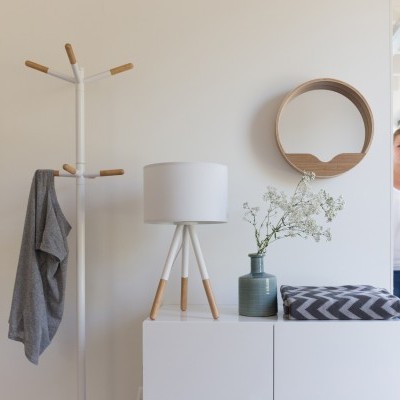 Decoração de interior com cabideiro, lâmpada, vaso com flores, manta e espelho redondo