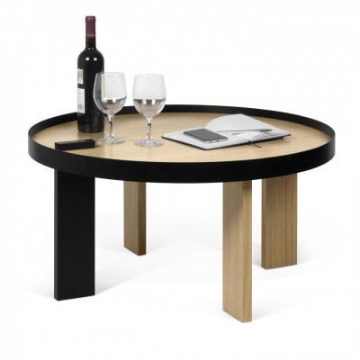 Mesa redonda baixa com tampo de madeira clara e quatro pés, um preto e três de madeira clara, com garrafa de vinho, duas taças, telemóvel e caderno