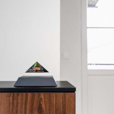 Piramide transparente colorida flutuando sobre base preta em móvel de madeira