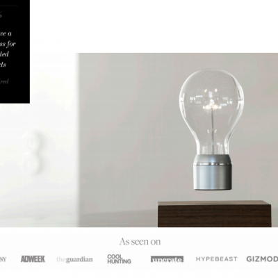 Lâmpada LED flutuante sobre base de madeira escura com texto e logótipos de publicações