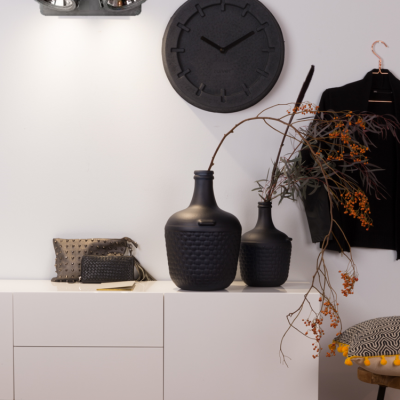 Móvel branco com objetos decorativos pretos, relógio preto na parede e roupa pendurada