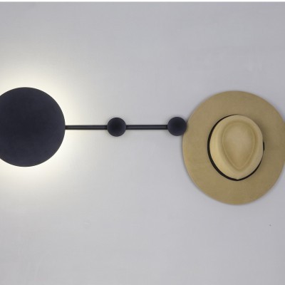 Arandela decorativa circular preta com chapéu bege pendurado numa parede branca