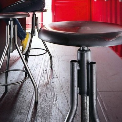 Banco alto preto com base metálica num piso claro junto a parede vermelha