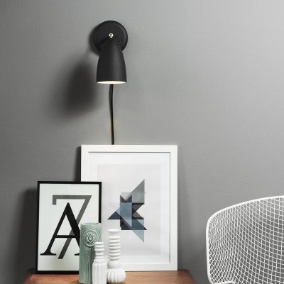 Luminária preta de parede, mesa de madeira com quadros e vasos, cadeira branca em malha metálica