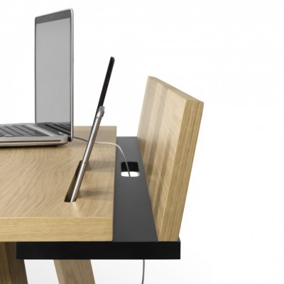 Mesa de madeira clara com computador portátil cinza e objeto preto com cabo branco