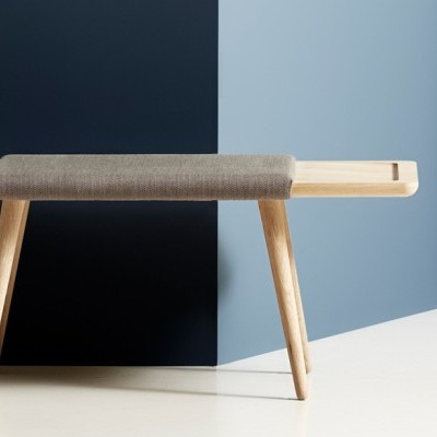 Banco de madeira clara com assento almofadado cinzento e planta num vaso preto