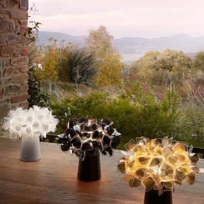 Três candeeiros de mesa decorativos com design floral abstrato em cima de uma superfície de madeira junto a uma janela com vista para a natureza