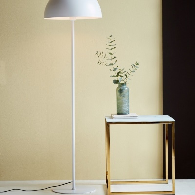 Candeeiro de pé branco moderno ao lado de mesa com estrutura dourada e vaso verde