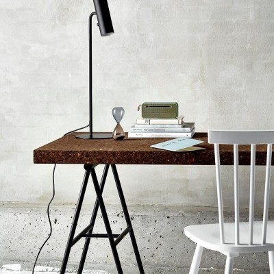 Mesa de cortiça com abajur preto e cadeira branca num ambiente minimalista