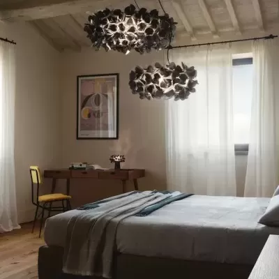 Quarto com cama cinza, lâmpadas florais negras penduradas e cadeira amarela ao lado da secretária