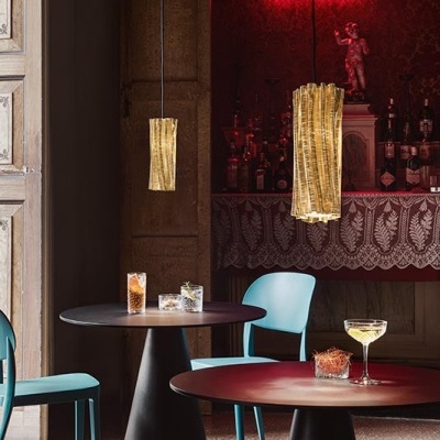 Mesa redonda preta com cadeiras azuis e pendentes dourados num ambiente com letreiro luminoso HOLY SPIRITS