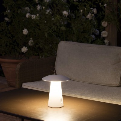 Luminária portátil branca em forma de cogumelo numa mesa de madeira em ambiente exterior junto a sofá bege
