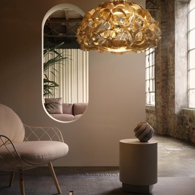 Lustre dourado pendente sobre mesa redonda em espaço com cadeira branca e parede de tijolos