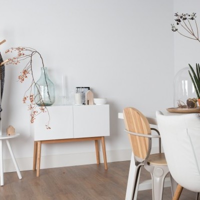 Sala de jantar com aparador branco, jarra de vidro, cadeira de madeira e metal, cabideiro com roupa