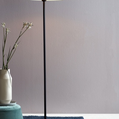 Candeeiro de pé preto com cúpula em semi-esfera junto a puff verde e vaso branco com flores