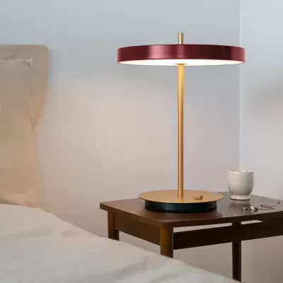Candeeiro de mesa dourado com cúpula vermelha e branca em mesa de madeira