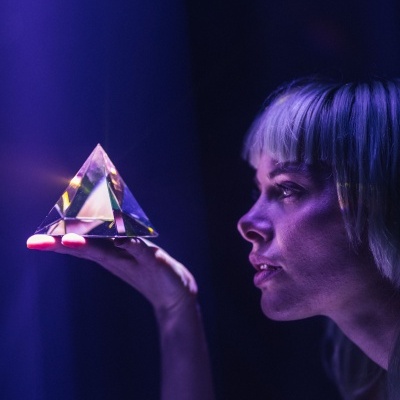 Mulher segurando uma pirâmide de cristal translúcida com luz roxa