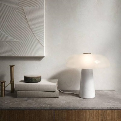 Abajur branco com cúpula de vidro fosco, livros cinzentos e caixa redonda numa superfície de pedra cinzenta