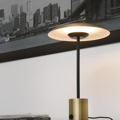 Candeeiro de mesa moderno em metal dourado e preto sobre mesa de madeira com livros e fotografia urbana na parede