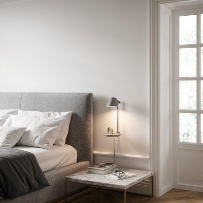 Quarto com cama cinzenta estofada, mesa com tampo em mármore e candeeiro de parede cinzento