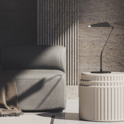 Mesa de apoio redonda bege em cerâmica com texturas, luminária preta minimalista e sofá cinza num ambiente interior.